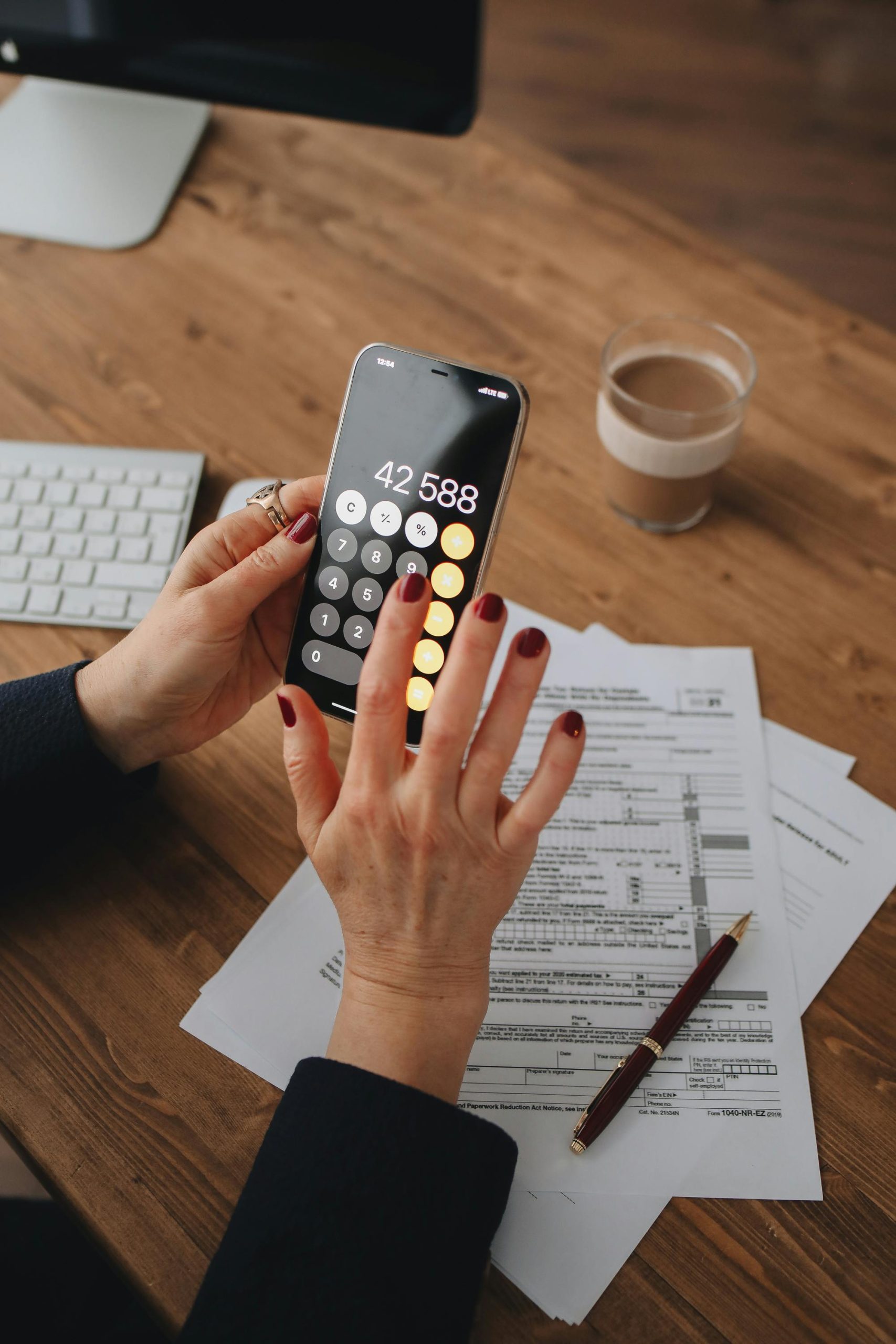 Person using a smartphone calculator while reviewing tax forms and financial paperwork on a desk.